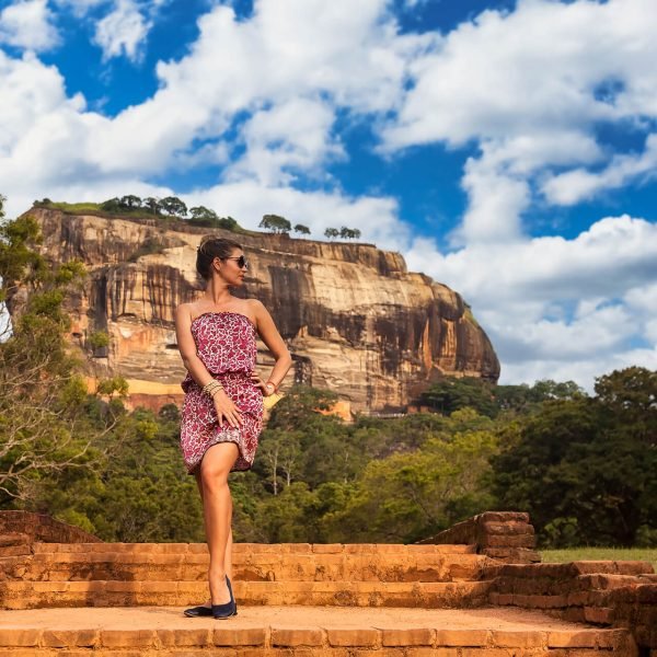 Young woman in sunglasses posing in front Sigiriya rock fortress at Sri Lankan sight landmark nature background. Cute lady traveler enjoying at tropical journey, Sri Lanka. Copy advertising text space